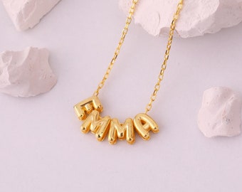 May include: Gold necklace with the name "EMMA" spelled out in bubble letters.