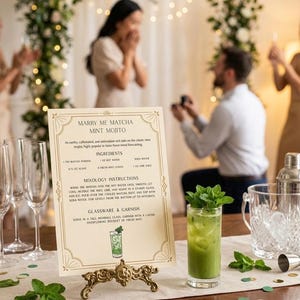 May include: A recipe card for a "Marry Me Matcha Mint Mojito" cocktail, displayed on a decorative stand. A green cocktail in a glass is visible. The card details ingredients and instructions. The background shows a proposal scene.
