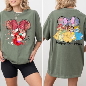 May include: Olive green t-shirt featuring a Minnie Mouse design with Ariel and the word "Ariel" on the front. The back of the shirt displays Disney princesses and the phrase "Happily Ever After".