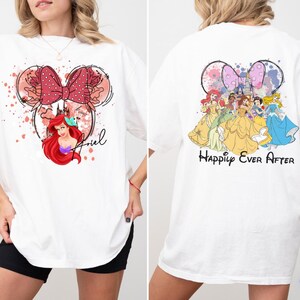May include: White t-shirt featuring a Minnie Mouse-inspired design with Ariel and a red bow on the front. The back of the shirt displays Disney princesses with the text "Happily Ever After".