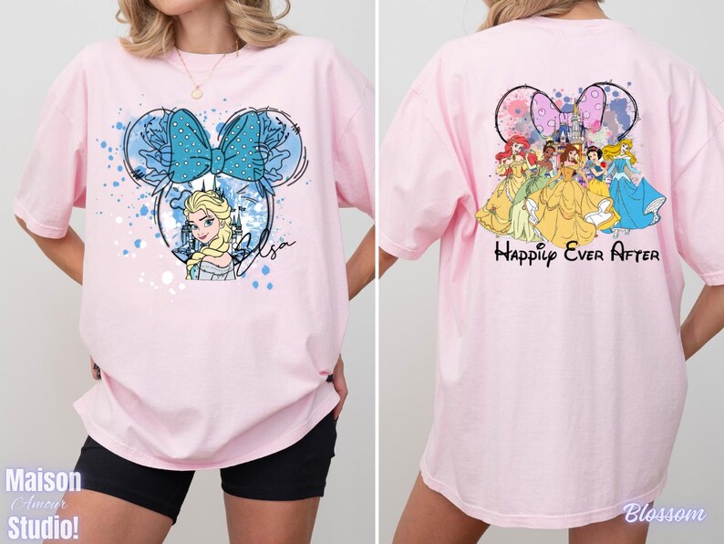 Pode incluir: Camiseta rosa claro com um design inspirado na Minnie Mouse com Elsa de Frozen, um la&ccedil;o azul e o nome "Elsa". A parte de tr&aacute;s da camiseta mostra princesas da Disney e o texto "Happily Ever After".