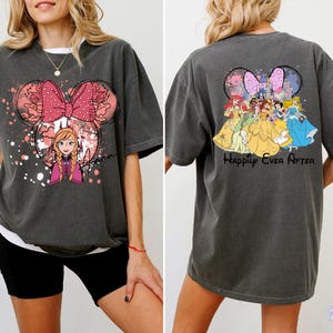May include: Dark grey t-shirt featuring a Minnie Mouse-shaped design with a pink bow and the character Anna from Frozen. The back of the shirt displays Disney princesses and the text "Happily Ever After".