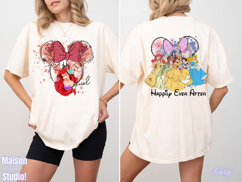 May include: Ivory-colored t-shirt featuring a Minnie Mouse-inspired design with Ariel from The Little Mermaid on the front. The back of the shirt displays Disney princesses with the text "Happily Ever After".