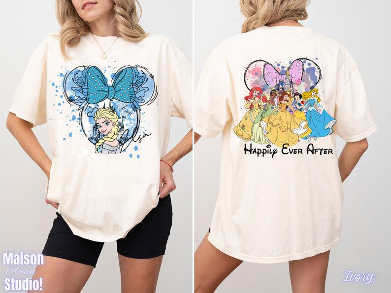 Pode incluir: Camiseta cor marfim com um design em forma de Minnie Mouse com Elsa de Frozen e um la&ccedil;o azul na frente. A parte de tr&aacute;s da camisa mostra princesas da Disney e as palavras "Happily Ever After".