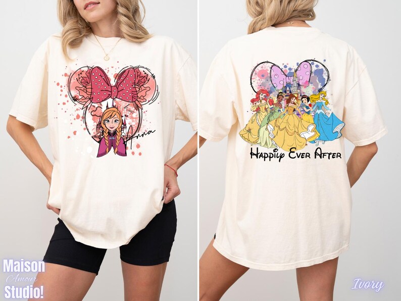 May include: Ivory-colored t-shirt featuring a Minnie Mouse-inspired design with Anna from Frozen on the front. The back of the shirt displays Disney princesses with the text "Happily Ever After". The shirt is a casual, oversized fit.