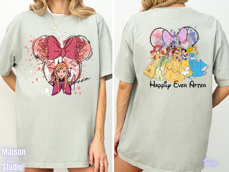 May include: A light green t-shirt featuring a Minnie Mouse-shaped design with Anna from Frozen. The front design includes a pink bow and the name "Anna". The back of the shirt displays Disney princesses with the text "Happily Ever After".