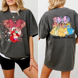 May include: Dark gray t-shirt featuring a Minnie Mouse design with a red bow, floral accents, and Ariel. The back of the shirt displays Disney princesses and the text "Happily Ever After".