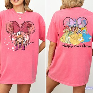 May include: Pink t-shirt featuring a Minnie Mouse-inspired design with Anna from Frozen on the front and a group of Disney princesses with the words "Happily Ever After" on the back. The shirt has short sleeves.