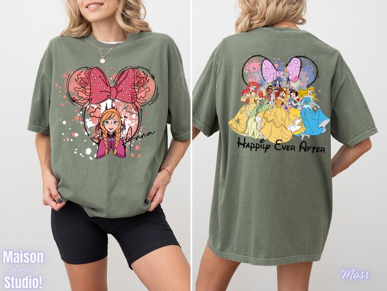 May include: Olive green t-shirt featuring a Minnie Mouse-inspired design with Anna from Frozen on the front. The back of the shirt displays Disney princesses and the text "Happily Ever After". The shirt has a relaxed fit.