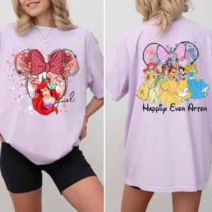 May include: A light purple t-shirt featuring a Minnie Mouse-inspired design with Ariel from The Little Mermaid on the front. The back of the shirt displays Disney princesses with the text "Happily Ever After". The shirt is a comfortable, oversized fit.