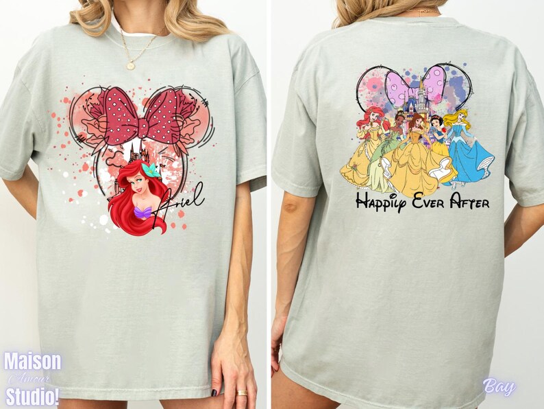 May include: A light green t-shirt featuring a Minnie Mouse-shaped design with Ariel, a red bow, and the name "Ariel". The back of the shirt displays Disney princesses and the words "Happily Ever After".