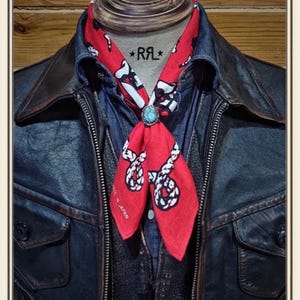 May include: A red bandana with a white rope print and the text "MADE IN JAPAN" secured with a turquoise stone slide. The bandana is worn over a dark blue denim shirt and a dark leather jacket. The text "DOUBLE RL & CO." and "RRL" are visible.