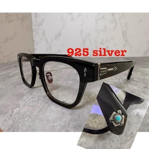 Può includere: Occhiali con montatura nera e dettagli a forma di freccia in argento 925 sulle aste. Una vista secondaria mostra un emblema a forma di aquila in argento con una pietra turchese centrale sul lato. Il testo 925 silver è visibile.