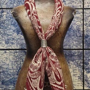 Puede incluir: Una bufanda con estampado de cachemira burdeos y blanco está drapeada sobre un maniquí. La bufanda se sujeta con un anillo plateado. Las palabras "COLOR-FAST COTTON" están impresas en la bufanda.