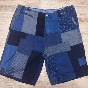 May include: Patchwork shorts featuring a variety of blue fabric panels in shades ranging from light denim to dark navy. The design includes solid sections, pinstriped fabric, and panels with a small white anchor print, finished with a button closure.