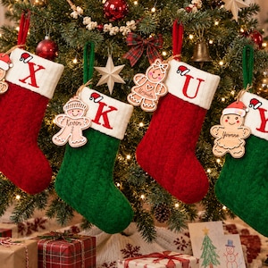 May include: Four cable-knit Christmas stockings in alternating red and green colors with white cuffs. Each stocking features a large red embroidered letter and a wooden gingerbread man ornament personalized with the names Xavier, Kevin, Ursula, and Yvonne.