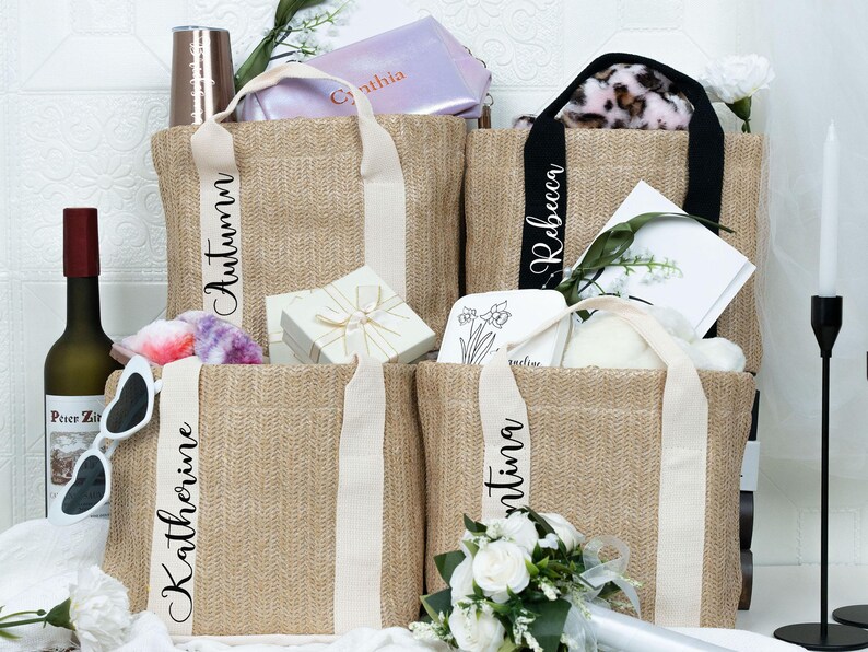 K&ouml;nnte beinhalten: Jute-Tragetaschen mit personalisierten Namen auf den Tr&auml;gern. Die Taschen sind mit Geschenken gef&uuml;llt, darunter eine Weinflasche, Sonnenbrille und eine Geschenkbox. Die Taschen haben cremefarbene Tr&auml;ger und sind mit Blumen dekoriert.