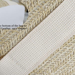 K&ouml;nnte beinhalten: Nahaufnahme einer gewebten Strohtasche mit cremefarbenem Riemen. Der Boden der Tasche ist aus PU-Leder. Der Riemen besteht aus einem dicht gewebten, hellen Stoff. Die gewebte Textur der Tasche ist sichtbar.