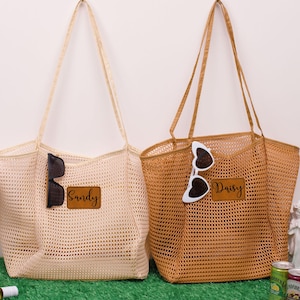 May include: Two mesh tote bags, one cream and one tan, with long handles. The cream bag has the name "Sandy" on a leather patch, and sunglasses. The tan bag has the name "Daisy" on a leather patch, and heart-shaped sunglasses.