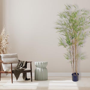 Può includere: Una poltrona marrone chiaro con un cuscino beige e una coperta marrone drappeggiata sul bracciolo. Un tavolino laterale verde chiaro con un design scanalato si trova accanto alla poltrona. Una grande pianta verde in vaso si trova nell'angolo della stanza.