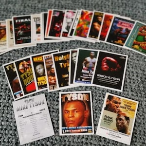May include: A collection of vintage trading cards featuring Mike Tyson, a famous boxer. The cards are in various colours and feature different images of Tyson, including a close-up of his face, a boxing match, and a poster for a fight. The cards are in good condition and would be a great addition to any sports memorabilia collection.