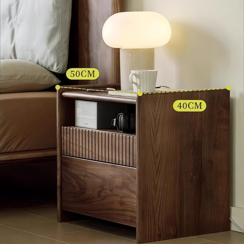 Puede incluir: Una mesita de noche de madera marr&oacute;n oscuro con dos cajones y un estante abierto. La mesita de noche tiene 40 cm de ancho y 50 cm de alto. Una l&aacute;mpara blanca con una pantalla blanca est&aacute; encima de la mesita de noche.