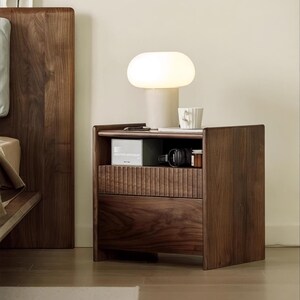 Puede incluir: Una mesita de noche de madera oscura con dos cajones y un estante abierto. La mesita de noche tiene una l&aacute;mpara blanca con una pantalla en forma de hongo en la parte superior. Hay una taza y un libro peque&ntilde;o en el estante.