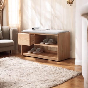 May include: A wooden shoe storage bench with a cushioned top, two shelves, and a drawer. The bench is made of light wood and has a natural finish. The shelves are empty and the drawer is open.
