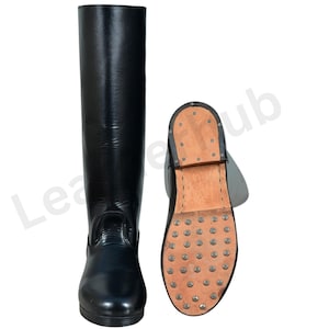 May include: Black leather riding boot with a matching sole. The sole is studded with metal cleats. The boot is tall, reaching the knee. The second boot is shown with the sole facing up.