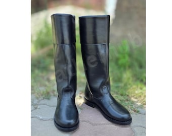 May include: A pair of black knee-high boots with a smooth finish, featuring a structured shaft, a rounded toe, and a low heel. The boots have a clean, minimalist design with vertical seam detailing along the front and sides of the leg.