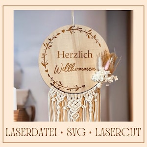 May include: A wooden round sign with the text "Herzlich Willkommen" in a decorative font, surrounded by a floral wreath. The sign is attached to a macrame dream catcher with a small bouquet of dried flowers.