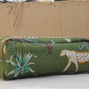 May include: Green rectangular cosmetic bag with a quilted texture. The bag features a jungle-themed print with white and yellow leopards, and green and blue plants. It has a zipper closure and a small fabric loop on the side.