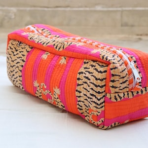 May include: A rectangular, quilted fabric bag with a white zip. The bag has a vibrant design with orange and pink stripes, and tiger print accents. A bright and colourful accessory.