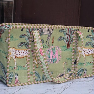 May include: A rectangular quilted tote bag in light green featuring a jungle print with cheetahs, zebras, and tropical plants. The bag has two handles and a pink embroidered letter M monogram centered on the front, finished with striped trim.