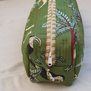May include: Green quilted fabric bag with a tropical print featuring toucans, trees, and other wildlife. The bag has a white zipper with pink and white striped trim. The bag is rectangular and appears to be a cosmetic or travel bag.