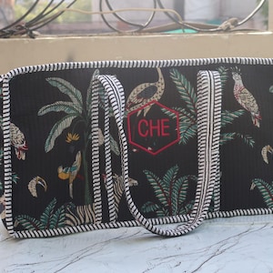 Puede incluir: Un bolso rectangular negro con un estampado tropical de palmeras, p&aacute;jaros y cebras. El bolso tiene asas y bordes a rayas blancas y negras. En la parte delantera hay un hex&aacute;gono rojo bordado que contiene las letras CHE en su interior.