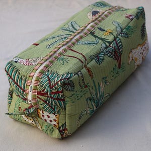 May include: A rectangular, quilted cosmetic bag with a green background and a tropical print featuring palm trees, flowers, and leopards. The bag has a white zipper and a decorative trim. The bag is approximately 9 inches long.