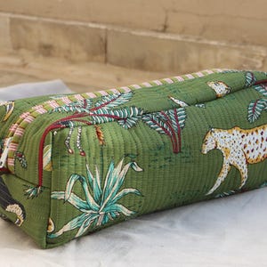 May include: Green quilted rectangular cosmetic bag with a jungle print featuring leopards, plants, and trees. The bag has a zipper closure and a pink and red striped trim. The bag is approximately 10 inches long.
