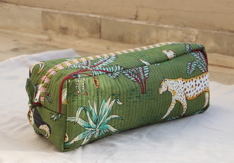 May include: Green quilted rectangular cosmetic bag with a jungle print featuring leopards, plants, and trees. The bag has a zipper closure and a pink and red striped trim. The bag is approximately 10 inches long.
