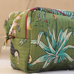 May include: Green quilted cosmetic bag with a botanical print featuring agave plants and other tropical elements. The bag has a rectangular shape with a zipper closure and a small fabric loop on the side.