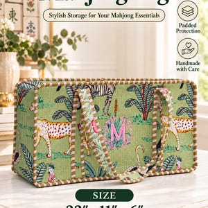 May include: A rectangular quilted Mahjong bag in light green featuring a print of cheetahs, zebras, and flamingos. The bag has a pink embroidered letter M, striped fabric trim, and two handles. Dimensions are 22 inches by 11 inches by 6 inches.