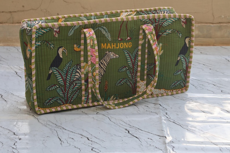 May include: Green tote bag with a tropical print featuring toucans, zebras, and palm trees for Mahjong game. The word "MAHJONG" is embroidered in gold.Mahjong Game Bag, Mahjong Lovers Gifts, You can keep your tiles, Rack, Folded mat inn Rack Bag and rolled mat in Mat Bag. Also this bag is perfect bag for gift for  Mahjong Lovers. Travel bag for Mahjong lovers.