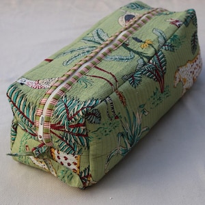 Puede incluir: Un neceser acolchado rectangular de tela verde claro con un patr&oacute;n repetitivo de plantas tropicales, hojas de palmera y animales moteados. El neceser incluye un cierre de cremallera blanco con un borde de tela a rayas rojas y blancas.