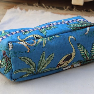 May include: A rectangular, blue fabric pouch with a tropical bird and foliage pattern. The pouch features a zipper closure and is likely used for storing cosmetics or small items. The design includes a mix of green, yellow, and white accents.