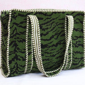 May include: Green corduroy tote bag with black tiger stripe pattern. The bag has two handles and is trimmed with white and green striped piping. The bag is rectangular in shape.