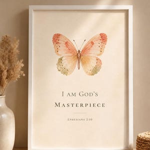 Puede incluir: Una lámina de arte enmarcada que presenta una mariposa de estilo acuarela en tonos melocotón y verde suave. Debajo de la mariposa, el texto dice "I AM GOD'S MASTERPIECE" en una fuente serif oscura, seguido de la cita "EPHESIANS 2:10" en letra más pequeña.