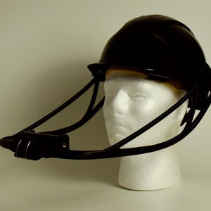 Puede incluir: Un casco negro con una visera negra unida a un marco de metal negro. El casco está en una cabeza de maniquí blanca.