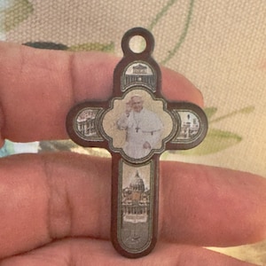 May include: A brown wooden cross with a picture of Pope John Paul II and the Vatican City on it.