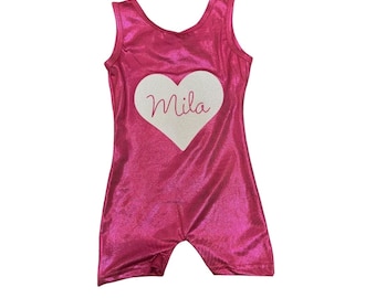 Puede incluir: Leotardo rosa con un corazón blanco y el nombre "Mila" impreso en él.