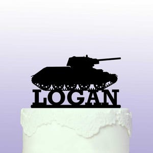May include: Black silhouette of a tank with the name Logan underneath. The tank is on a white cake.